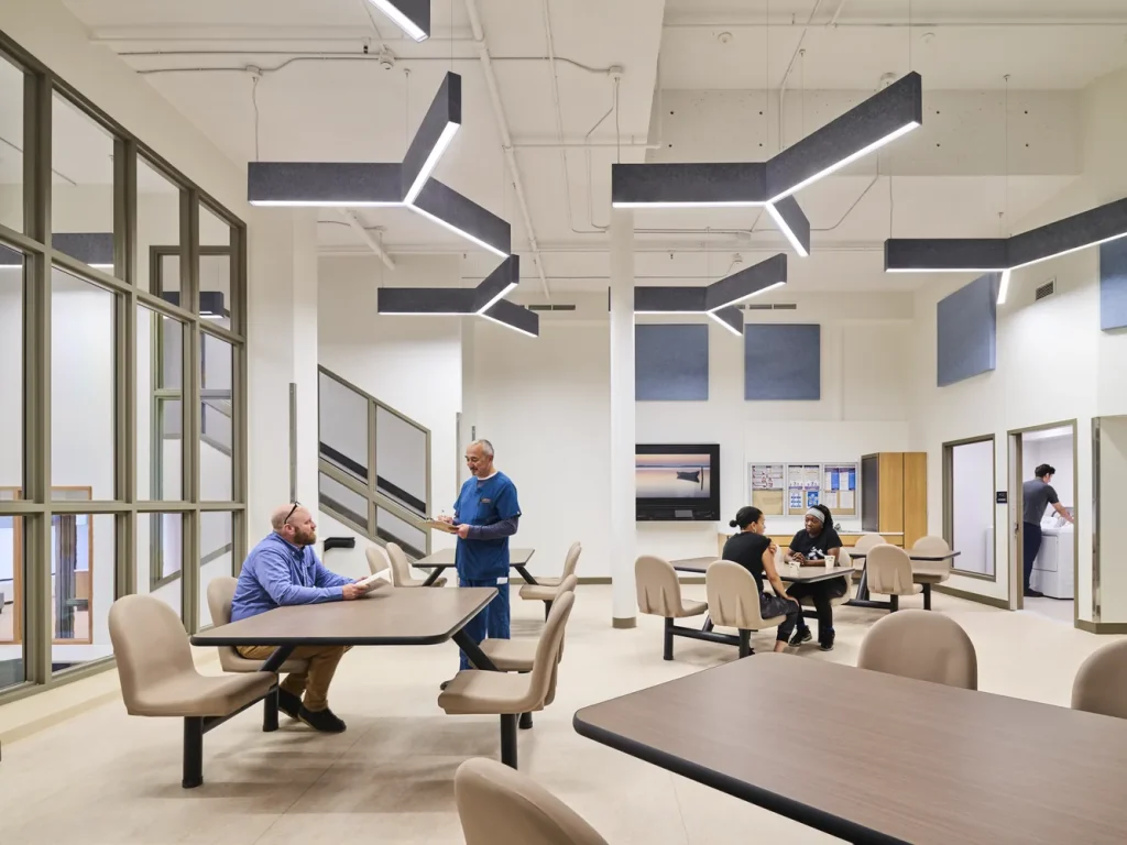 Dining and activity room with staff and patients seated at tables beneath linear pendant lighting