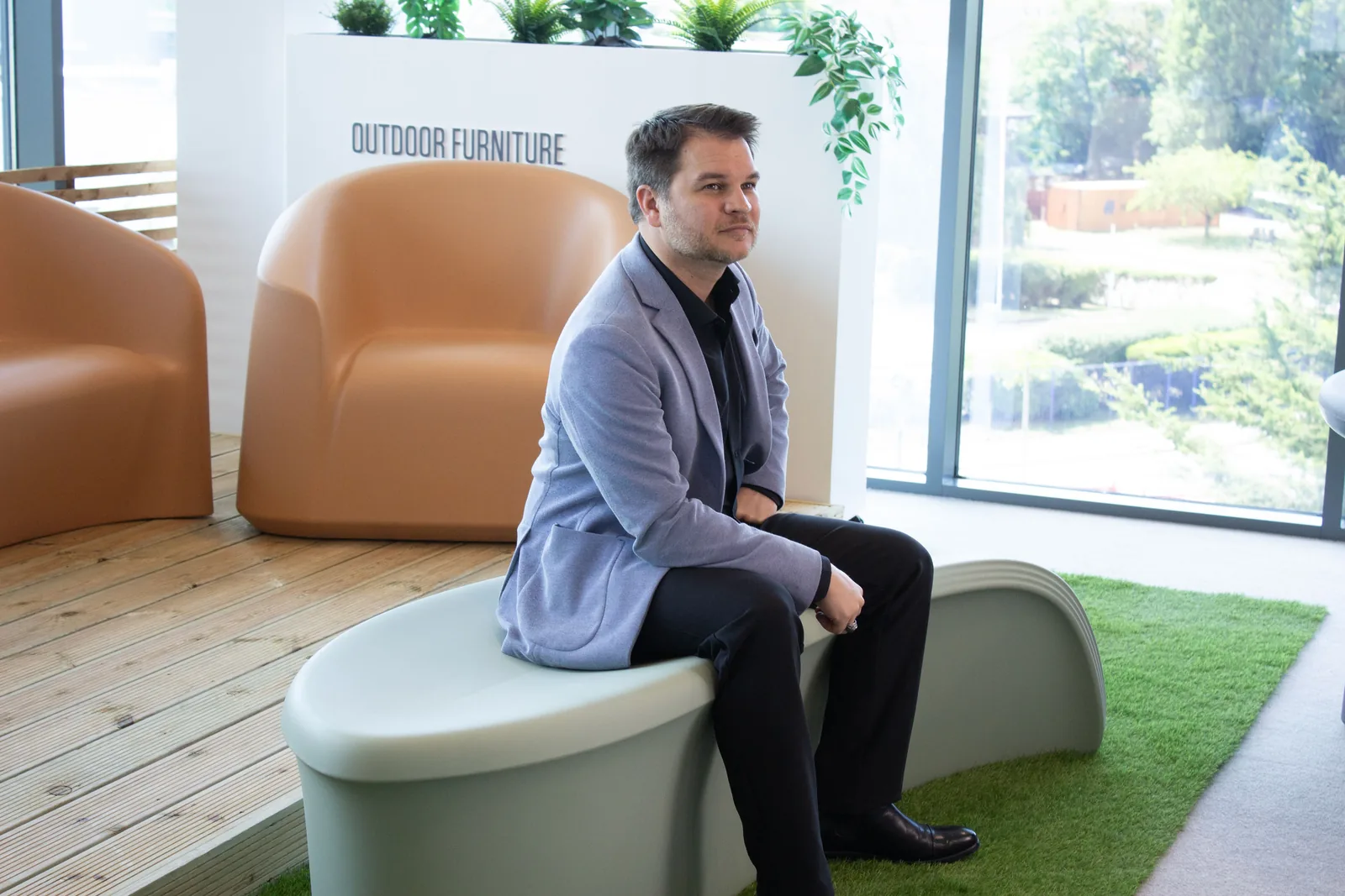 Stephen Parker seated on a curved Blossom Bench prototype beside a window.